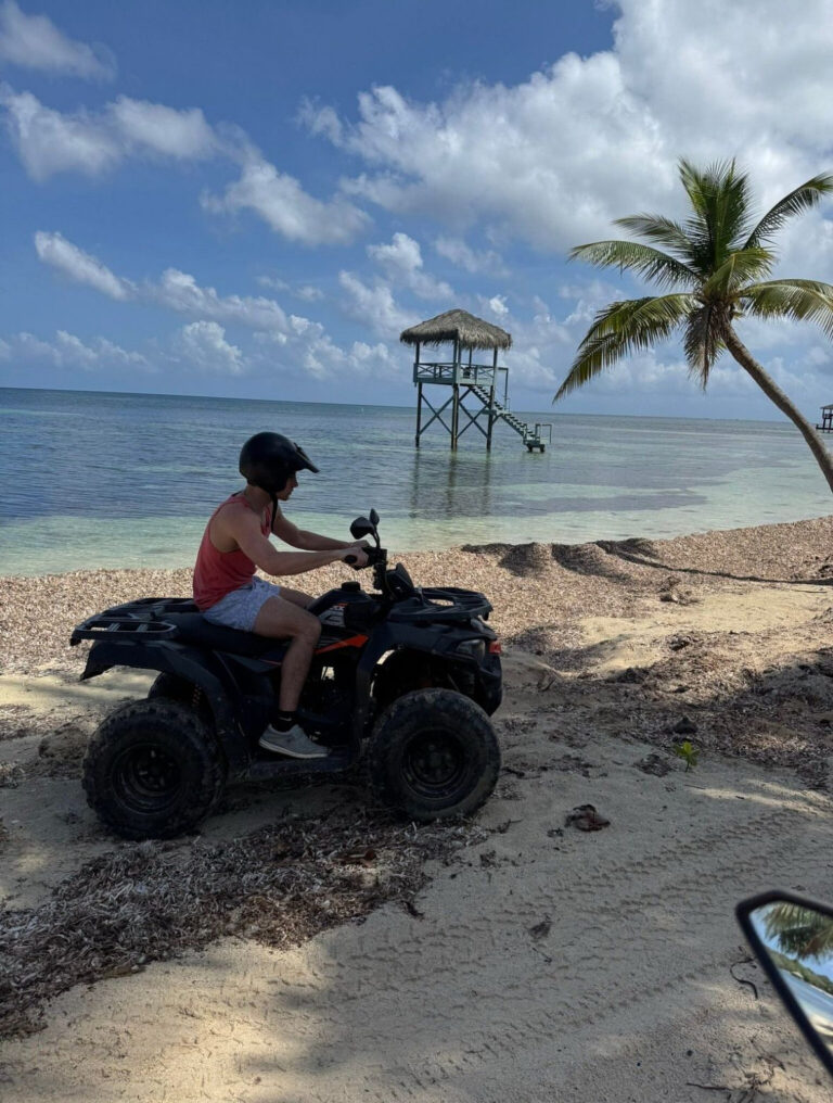 Guest riding an ATV on a Roatán beach next to a lifeguard tower