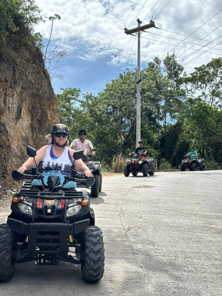 Guests riding ATVs on a hillside road in Roatán